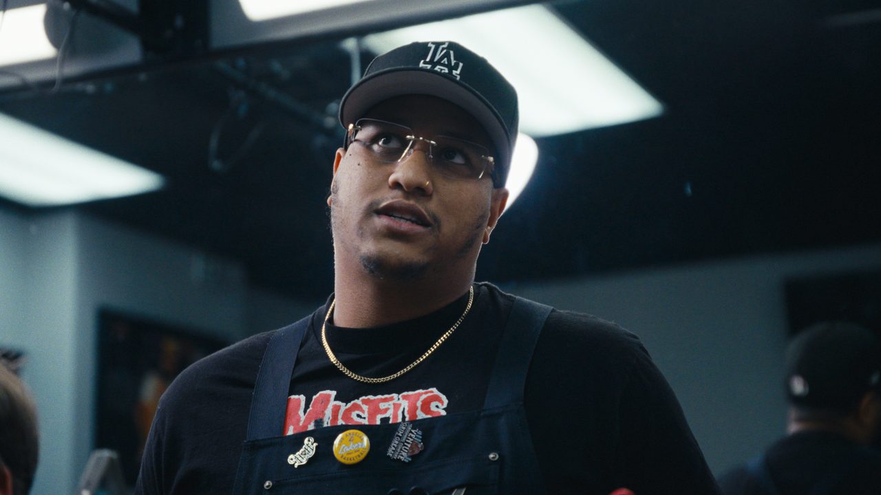 Corey Ernest, in a black cap and glasses, looks up in his barbershop under circular ring lights.