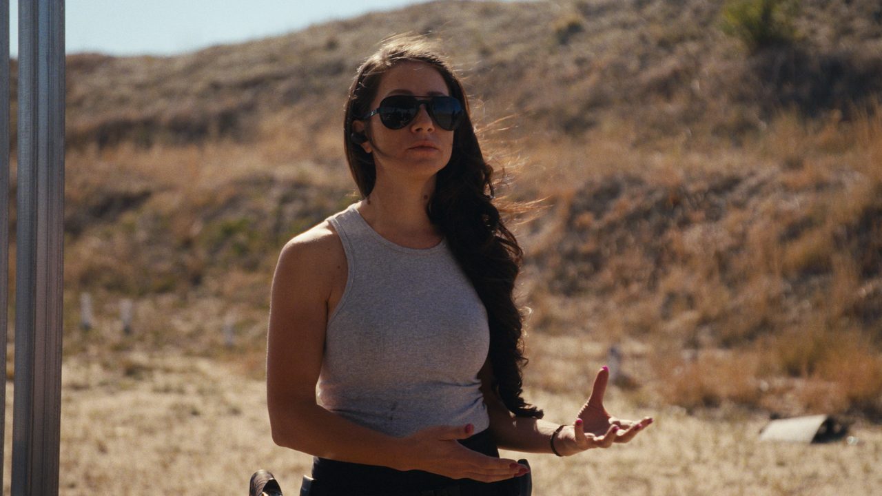 Melissa Flanell, in sunglasses with long dark hair, gestures as she talks on a dry, grassy hillside.