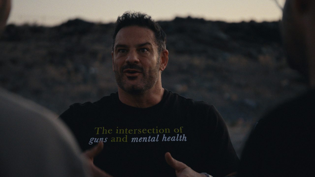 Mike Sodini talks at dusk in a T-shirt that reads 'The intersection of guns and mental health'.